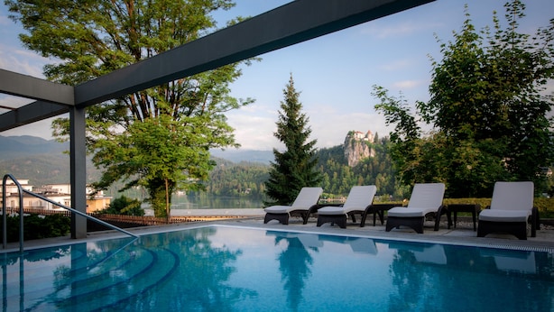 Piscina con sillas de descanso, rodeada de árboles y vista a la montaña.