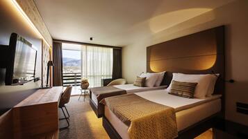 A hotel room with a large bed, a desk, and a chair. There is a TV mounted on the wall and a window with curtains.