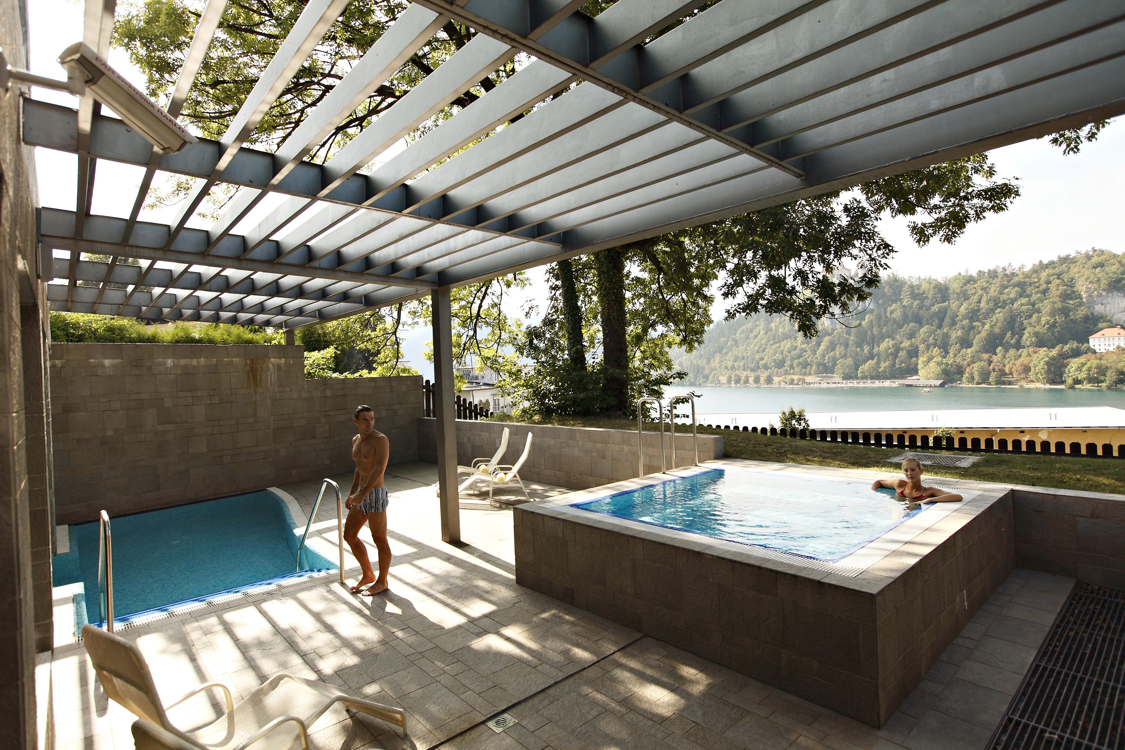 A pool area with a hot tub, lounge chairs, and a view of a lake.