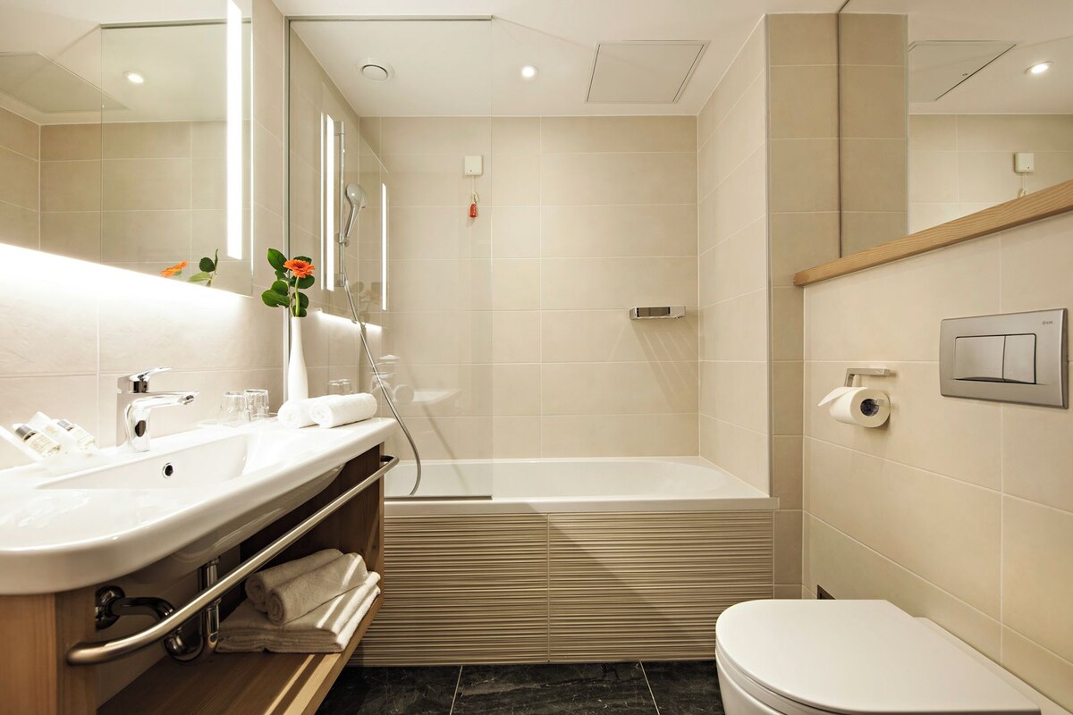 Un baño moderno con lavamanos, espejo, ducha e inodoro.