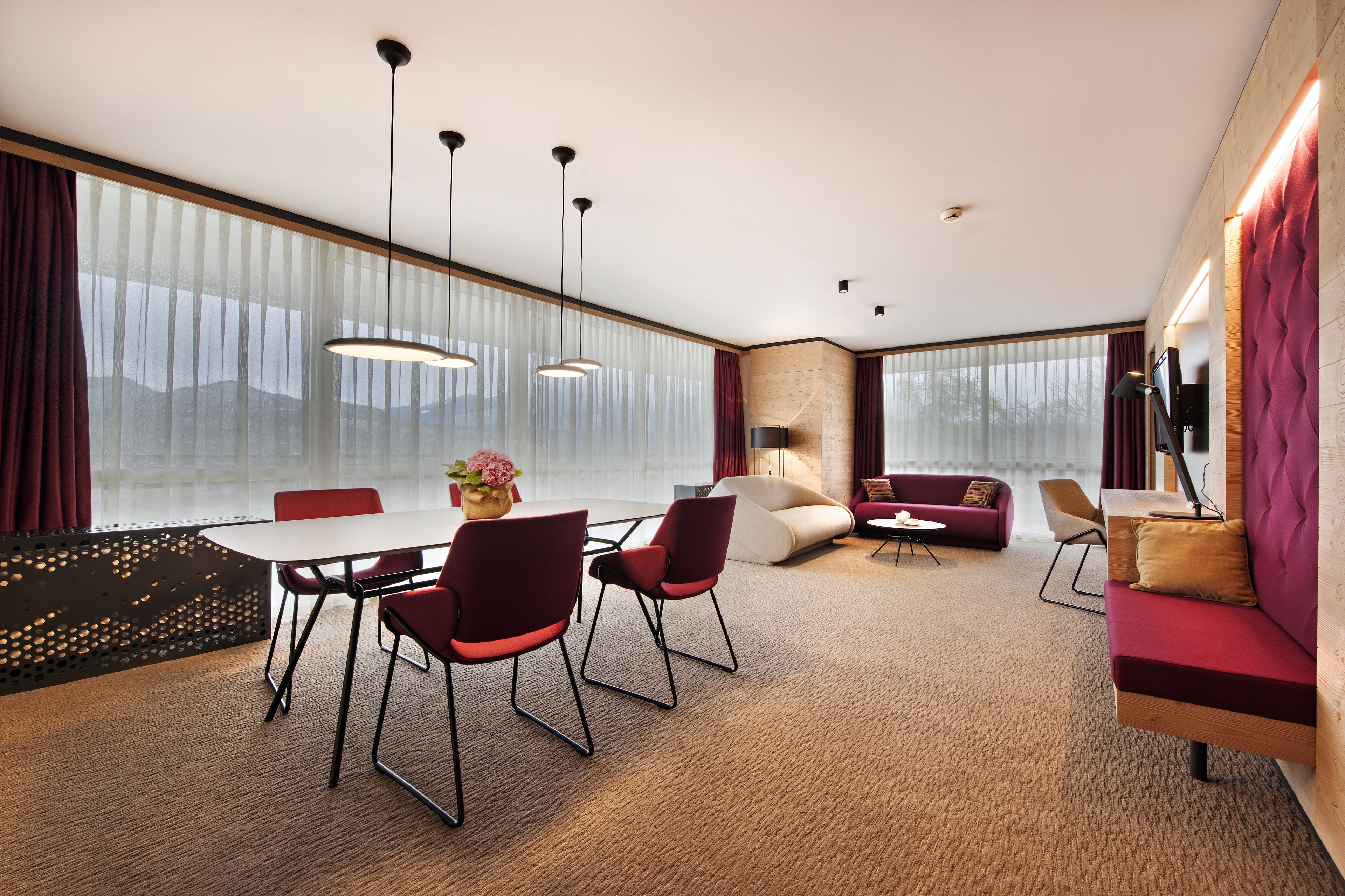A modern hotel room with a dining area, a sofa set, and a large window with curtains.