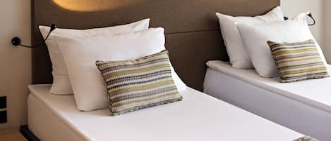 Een hotelkamer met twee bedden, elk voorzien van witte beddengoed en een gestreept kussen.
