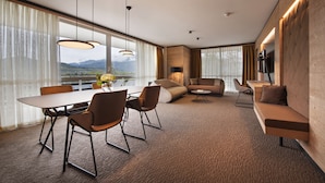 Una habitación de hotel moderna con comedor, sofá y televisor montado en la pared.