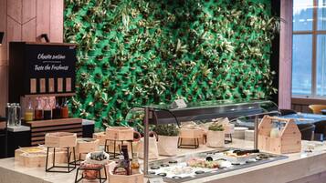 Zona de bufé con diversos alimentos y una pared decorada con follaje verde.