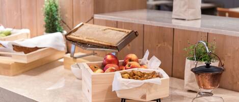 Una encimera de madera con diversos alimentos, incluyendo manzanas y aperitivos fritos, y una olla de cobre sobre un soporte.