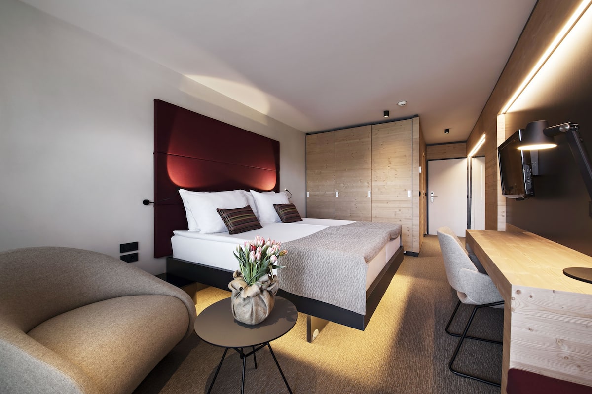 Une chambre d’hôtel moderne comprenant un lit, un canapé, une petite table avec des fleurs, un bureau et une armoire.