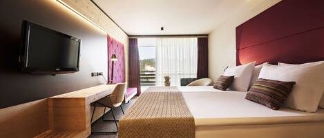 A modern hotel room with a large bed, a desk, a chair, and a TV.