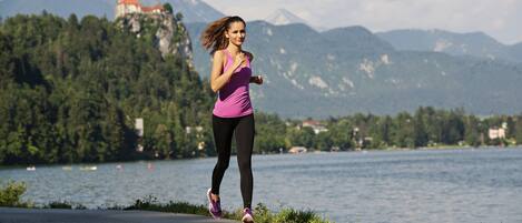 Una mujer trotando sobre un sendero pavimentado, con un lago y montañas al fondo.