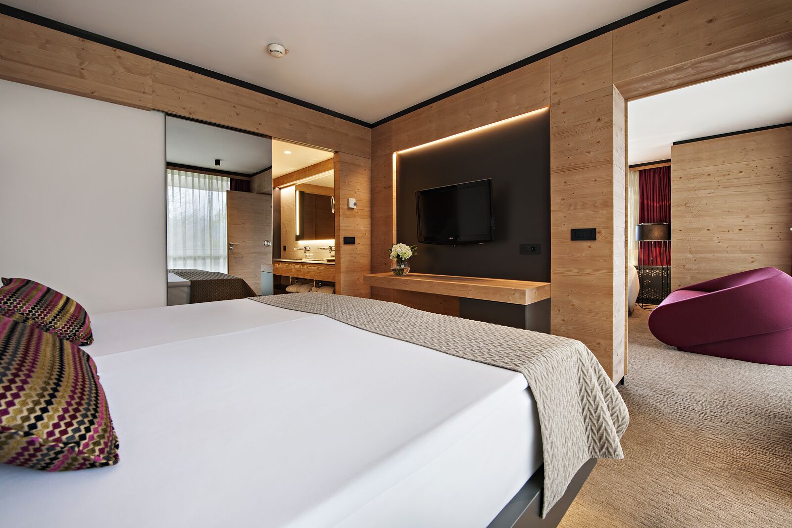 Ett modernt hotellrum med en stor säng, en TV, en vägg med träpanel och en röd stol.