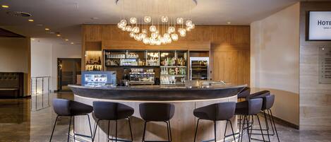 A modern bar area with a central bar counter, multiple stools, and a variety of bottles and glasses on shelves.