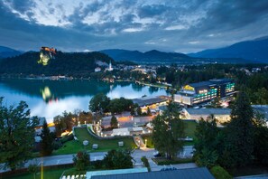 A hotel with a modern design, located near a lake with a castle on a hill.