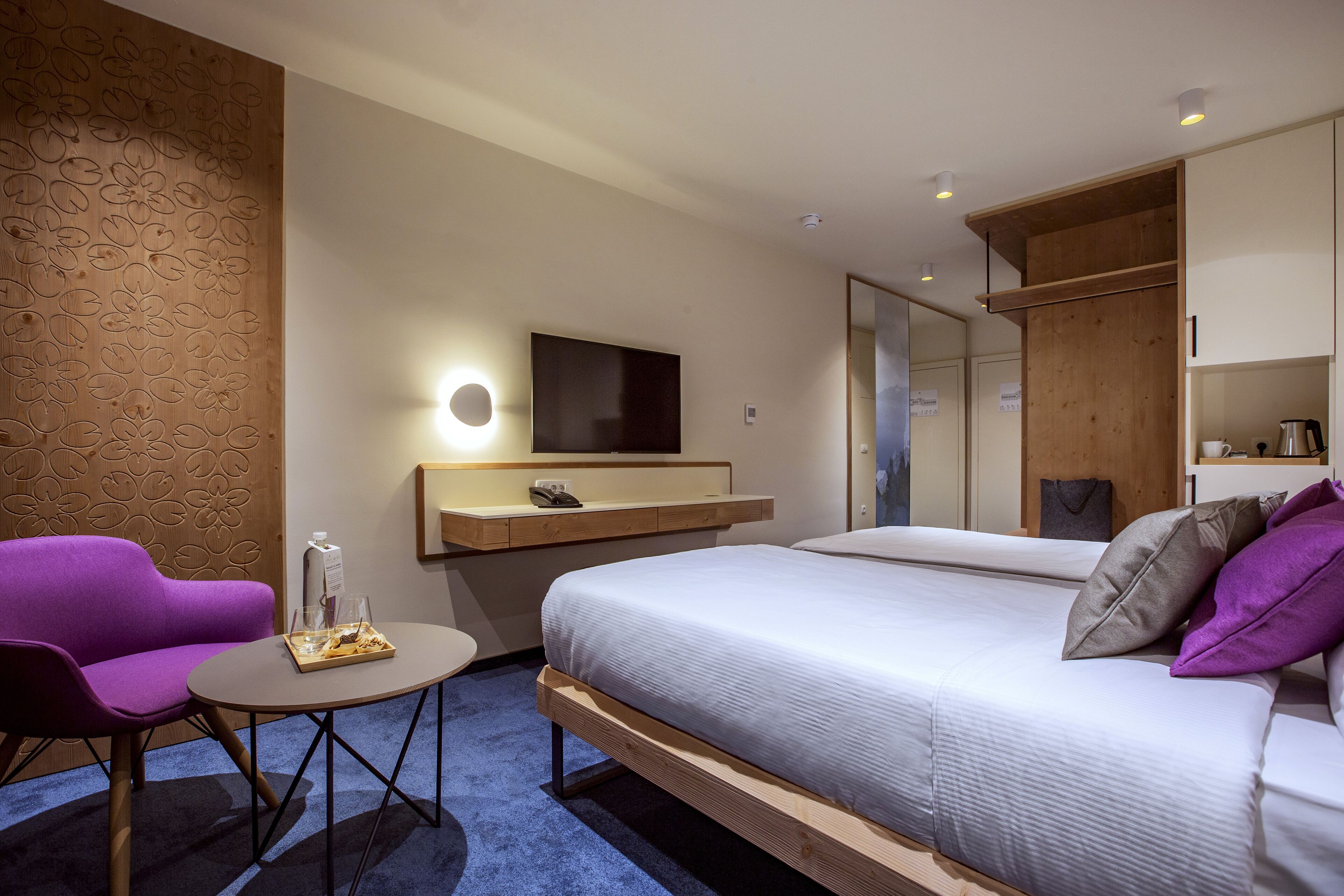 Een moderne hotelkamer met een bed, een sofa, een kleine tafel, een televisie en een houten accentmuur.
