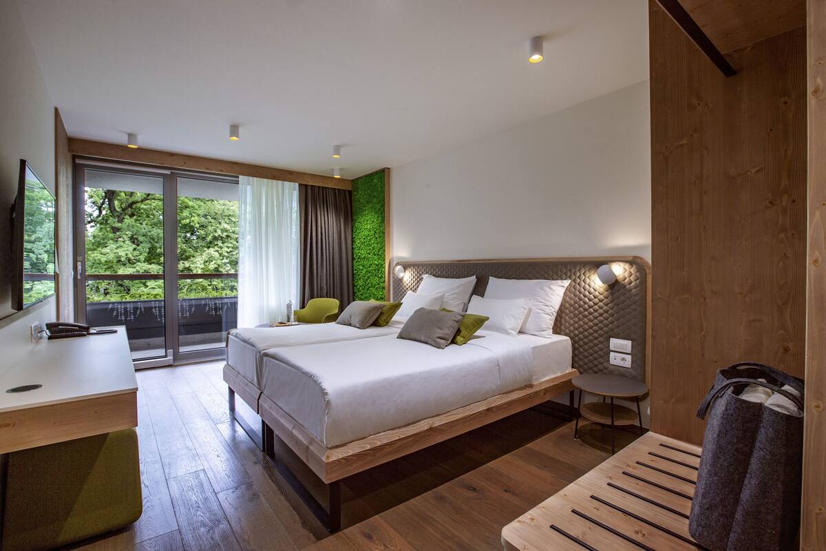 Een moderne slaapkamer met een groot bed, een bureau en uitzicht op groen.