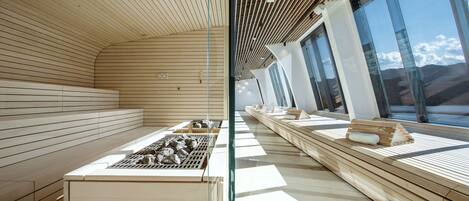 Ein modernes Interieur mit Holzbalken an der Decke, einer langen Sitzbank mit Grill und Steinen, und großen Fenstern mit Blick.