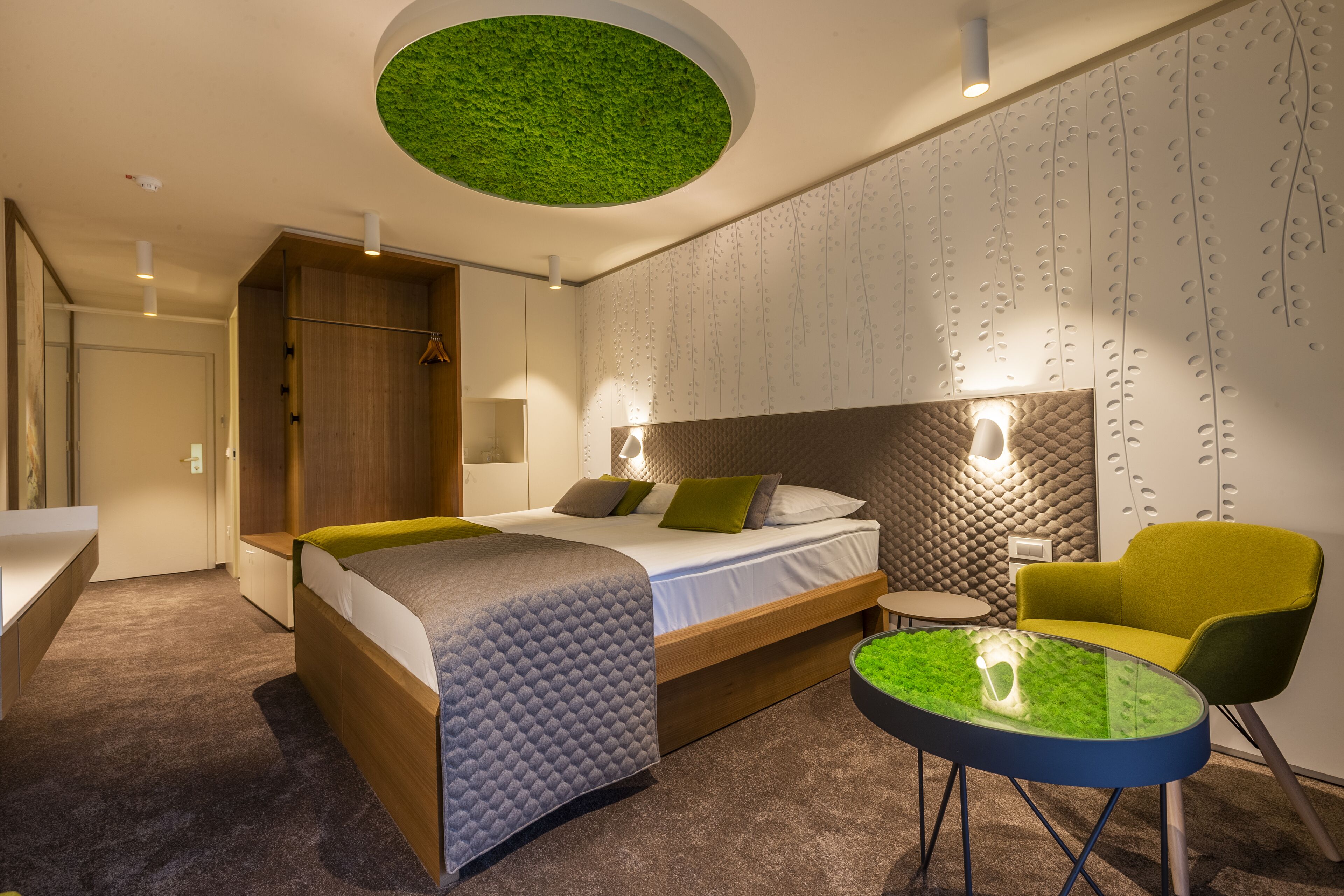 A modern bedroom with a bed, a small table, a chair, and a unique ceiling design.