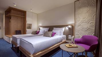 Ein Hotelzimmer mit einem großen Bett, einem kleinen Tisch, einem violetten Stuhl und einem Holzschrank.