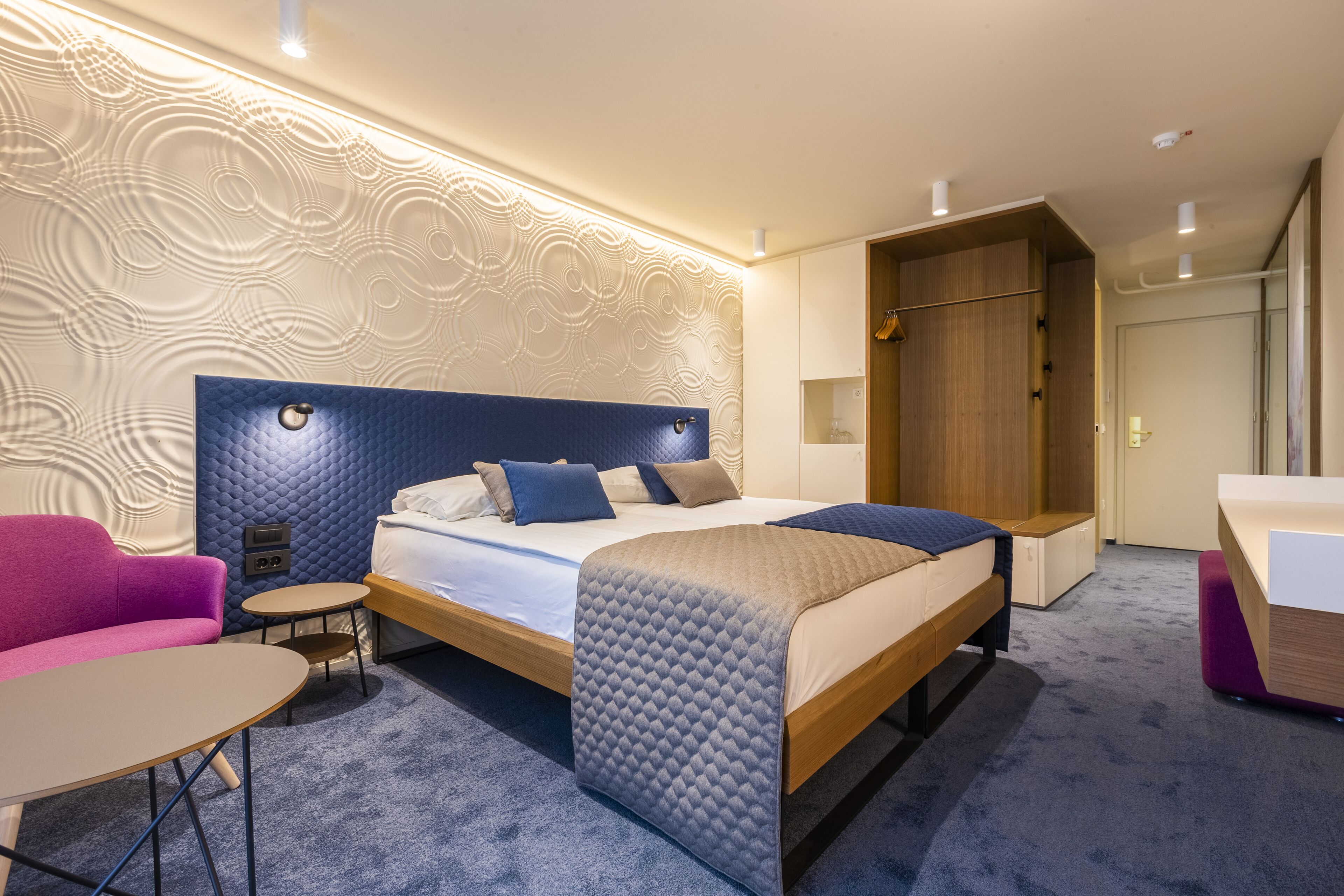 Ett modernt hotellrum med en stor säng, ett litet runt bord, en soffa och en garderob.