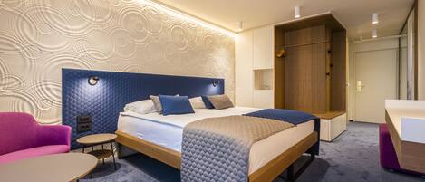 A modern hotel room with a large bed, a small round table, a sofa, and a wardrobe.