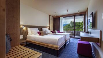A modern hotel room with two beds, a desk, a balcony, and a large window offering a scenic view.