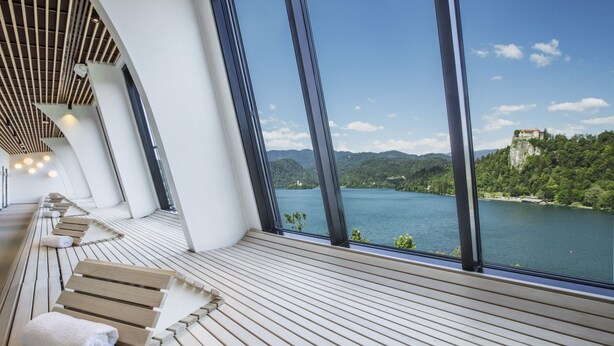 Ein moderner Wellnessbereich mit Holzliegen und einem großen Fenster mit Blick auf einen See und Berge.