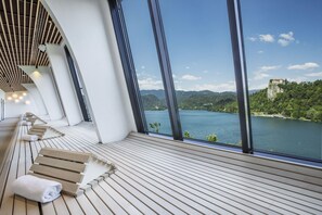Un espace spa moderne avec des chaises longues en bois et une grande fenêtre donnant sur un lac et des montagnes.