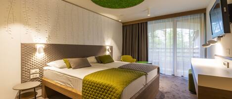A modern hotel room with a large bed, a desk, a chair, and a television.