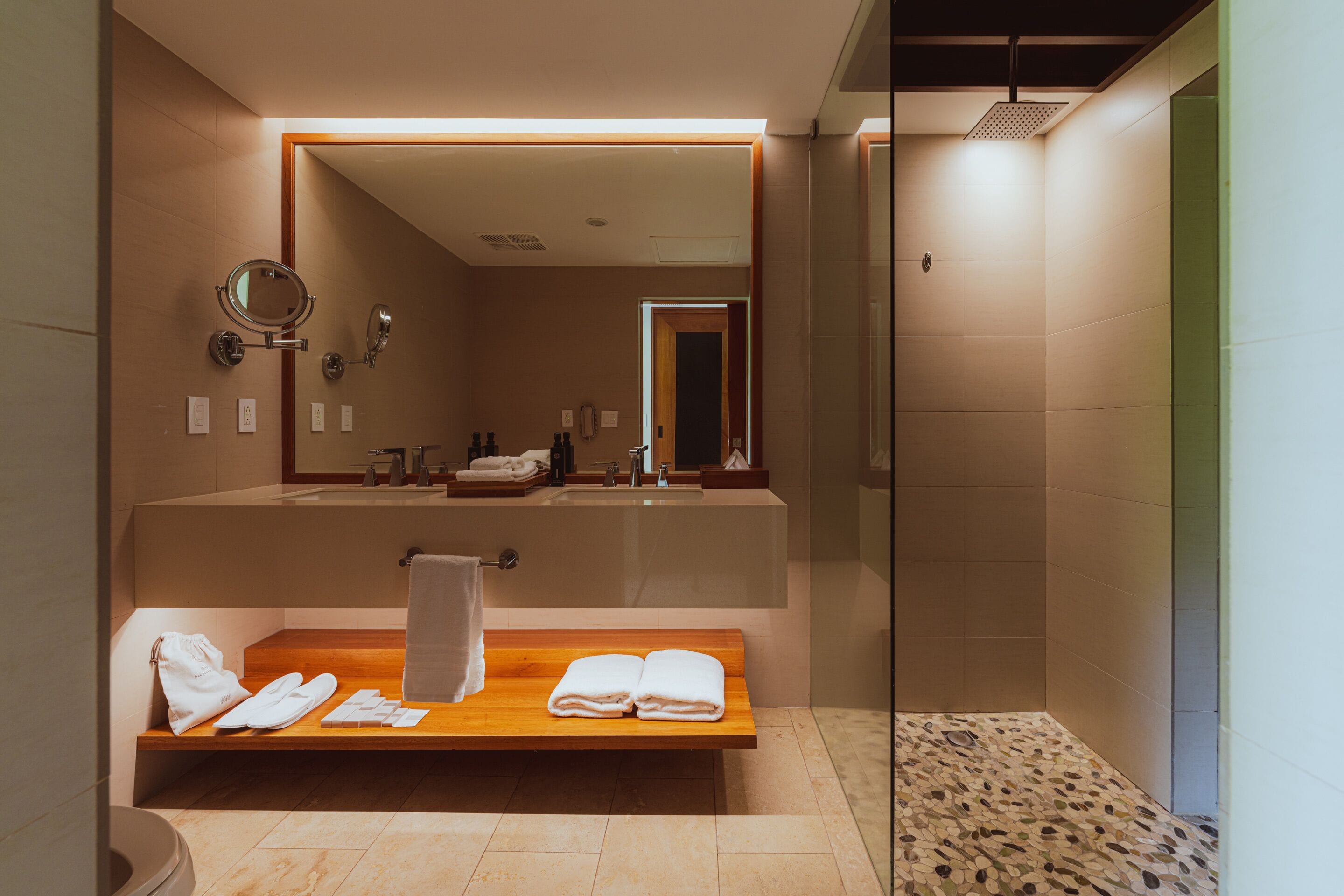 A modern bathroom with a wooden bench, a large mirror, and a shower area.