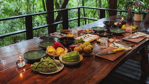 A wooden dining table set with various dishes and fruits, surrounded by lush greenery.