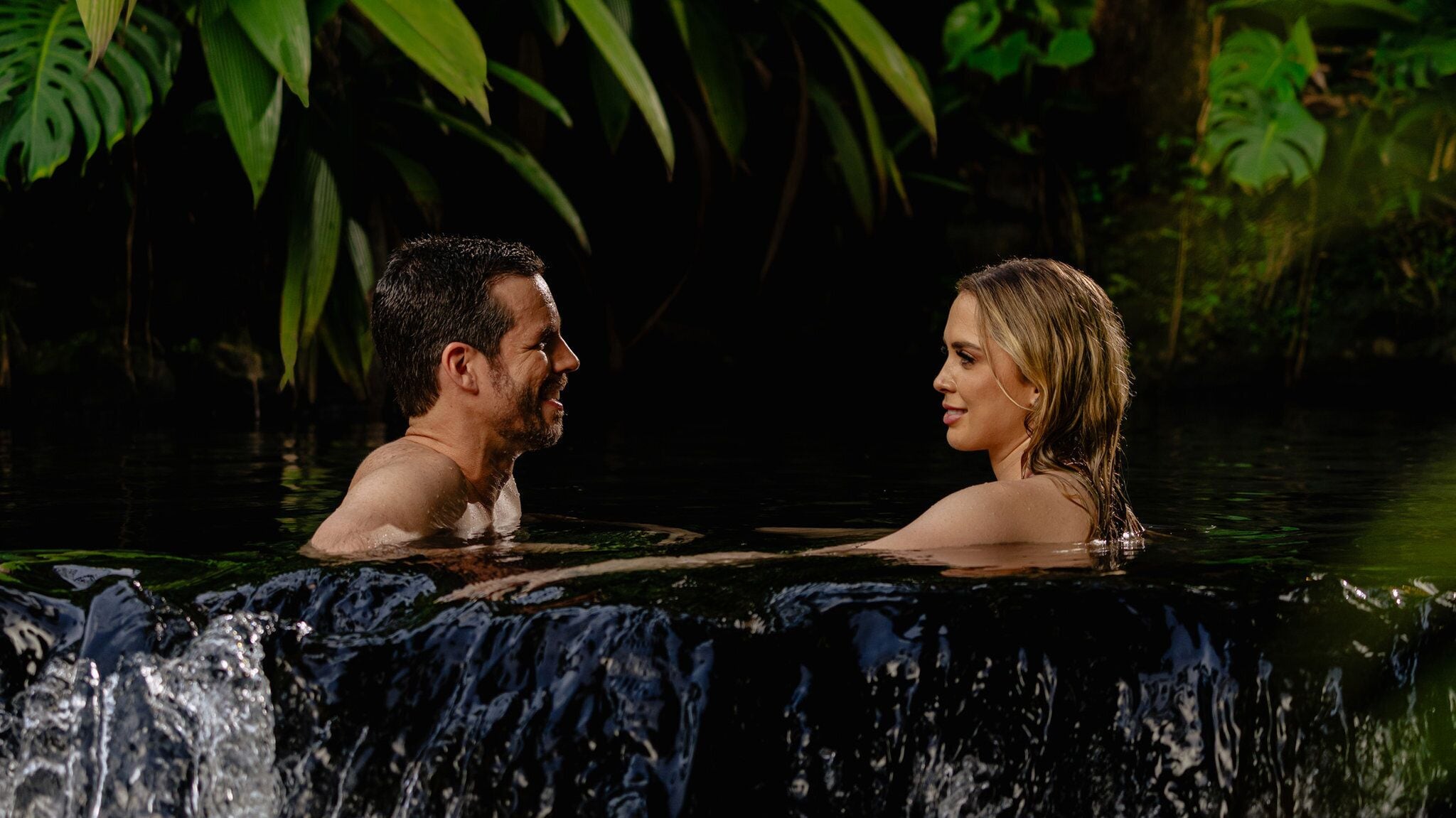 A couple in a hot tub surrounded by lush greenery.