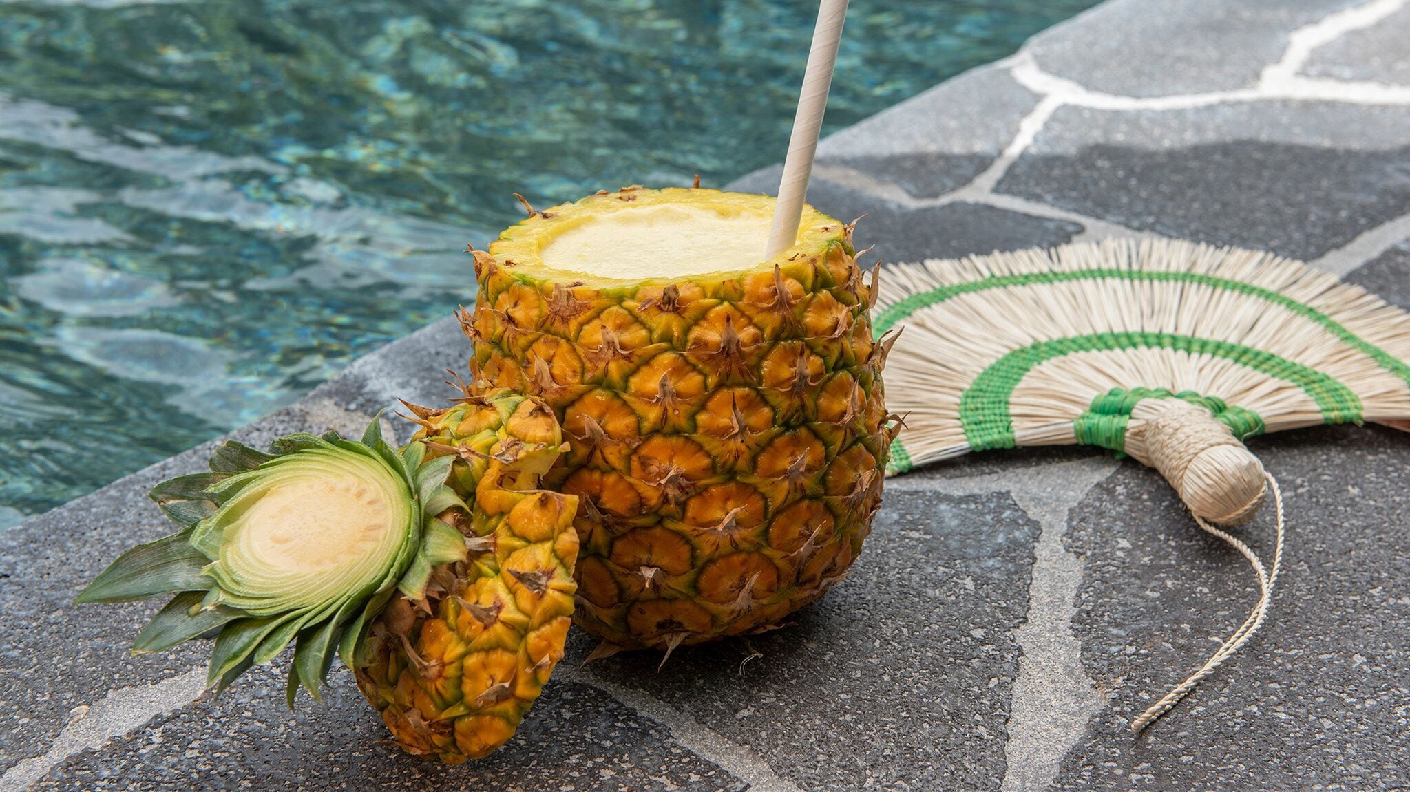 Una piña con pajita, sobre una superficie de piedra cerca de una piscina.