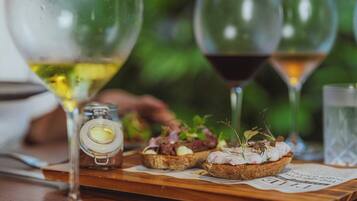Una mesa de madera con dos copas de vino, un frasco pequeño y dos rebanadas de pan con condimentos.