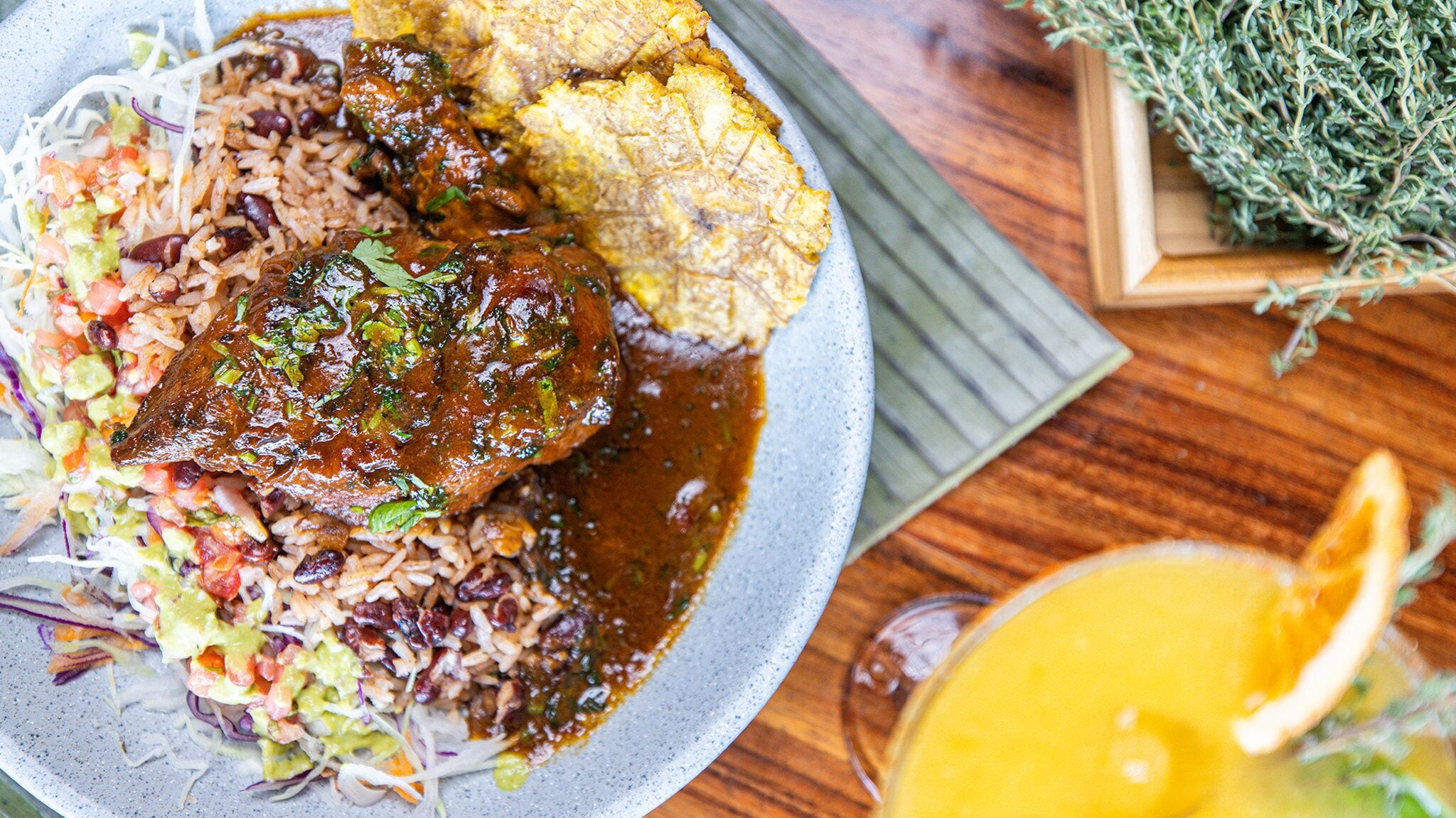 A plate of food with rice, beans, and a meat dish, accompanied by a side of coleslaw and a slice of bread.