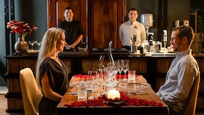 A dining table set with multiple wine glasses, a candle, and rose petals.