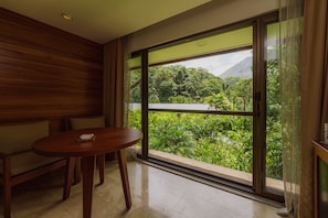 A room with a large window offering a view of lush greenery and a mountain.