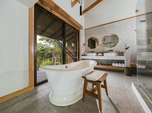 A modern bathroom with a freestanding bathtub, a wooden stool, a glass shower enclosure, and a large mirror.