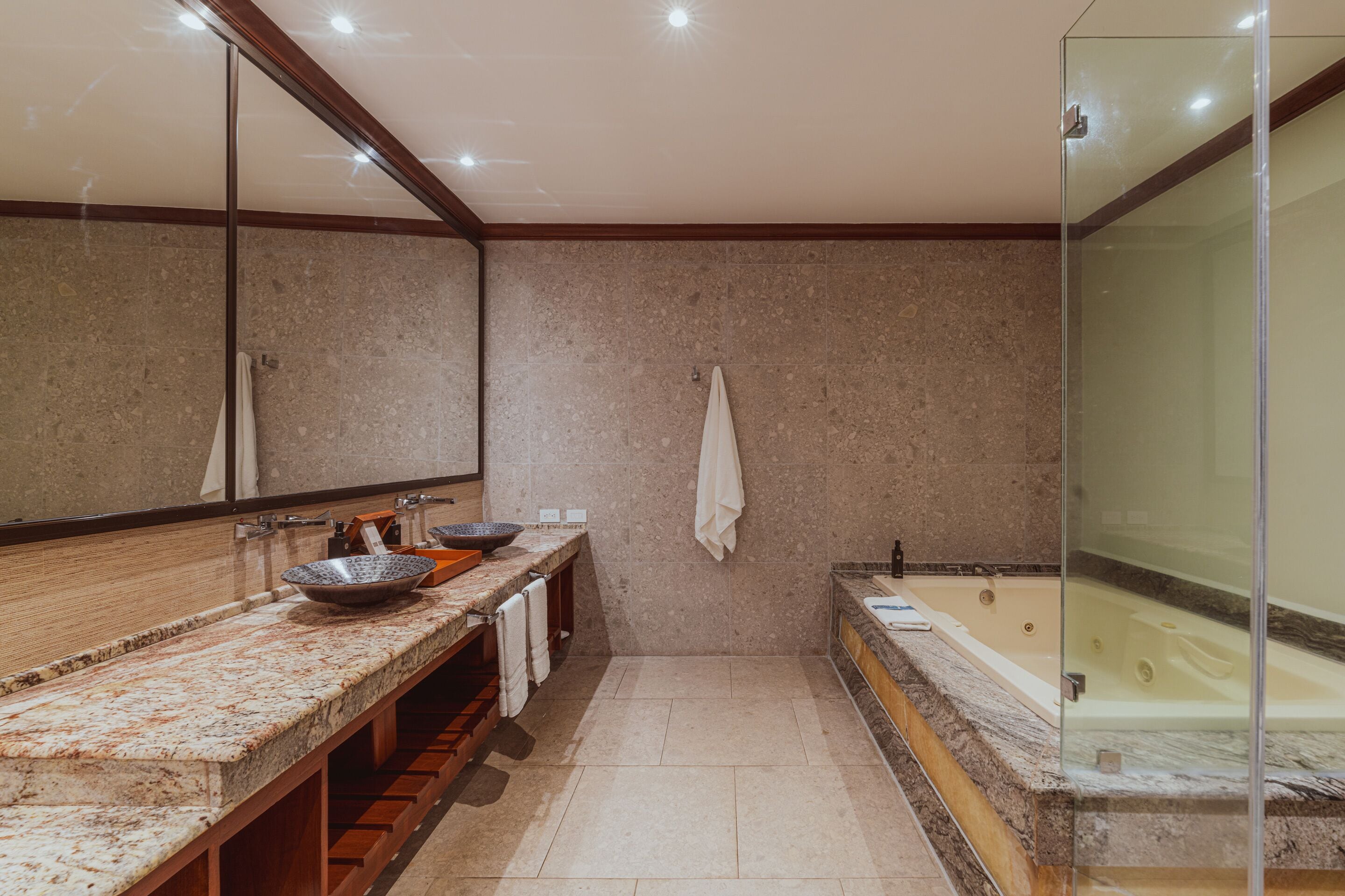 A modern bathroom with a large mirror, a granite countertop, a bathtub, and a glass shower enclosure.