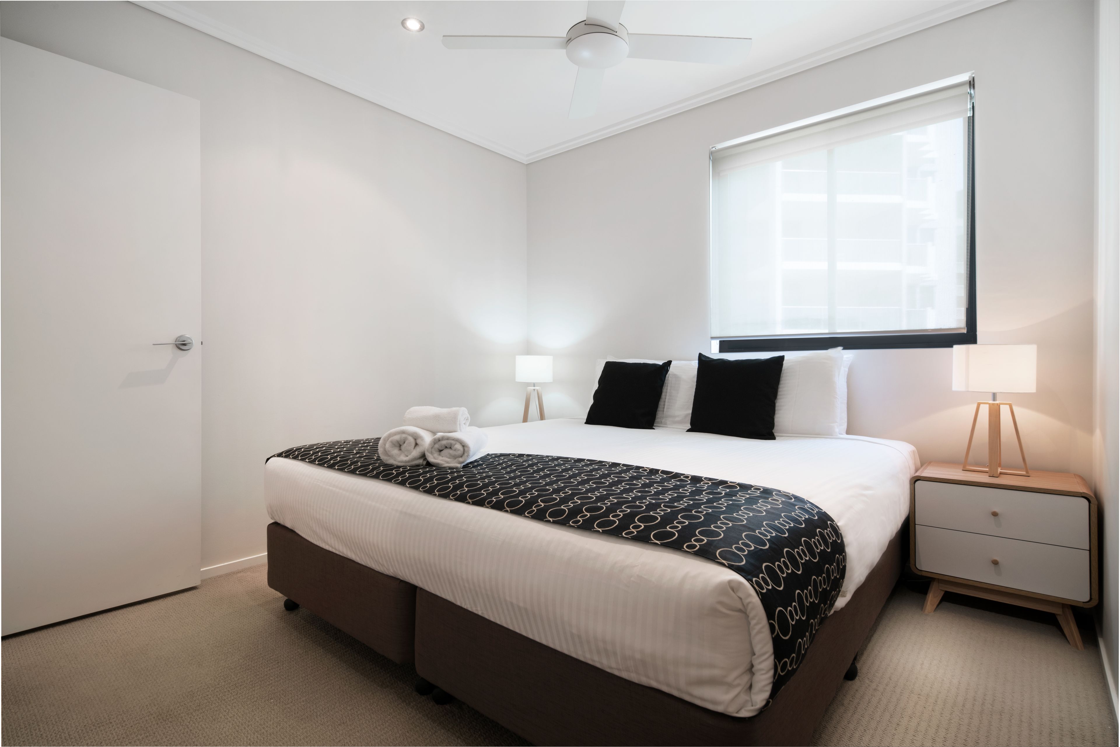 A bedroom with a bed, bedside tables, a ceiling fan, and a window.
