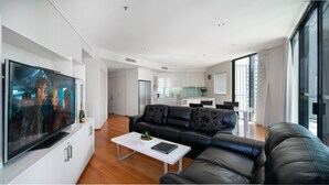 A modern living room with a flat-screen TV, a black leather sofa, and a white coffee table.