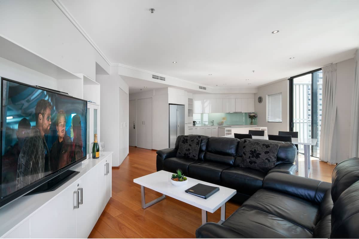 Una sala de estar moderna con un televisor de pantalla plana, un sofá de cuero negro y una mesa de centro blanca.