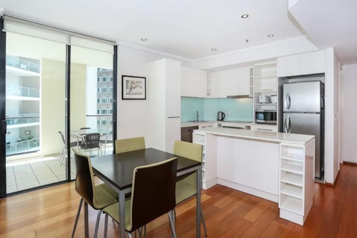 A modern kitchen with white cabinetry, a dining table with chairs, and a refrigerator.