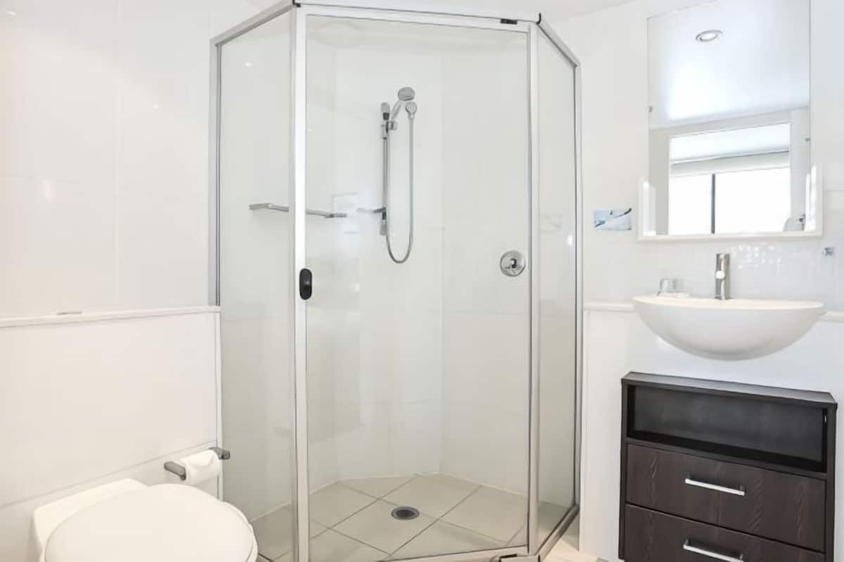 Un baño con ducha de vidrio, lavamanos blanco y tocador oscuro.