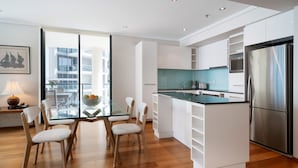 A modern kitchen with white cabinetry, a stainless steel refrigerator, and a glass dining table with chairs.