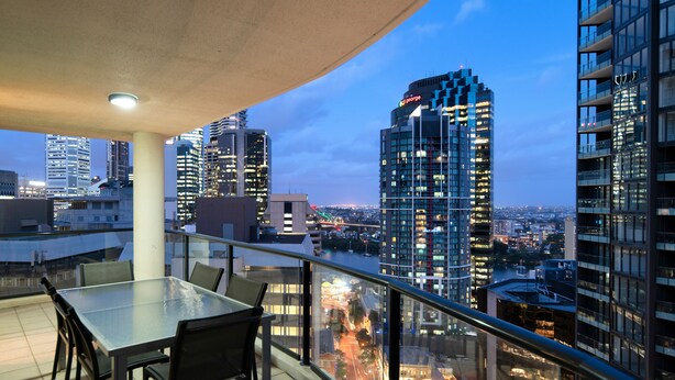A balcony with a table and chairs, overlooking a cityscape with tall buildings and a river.