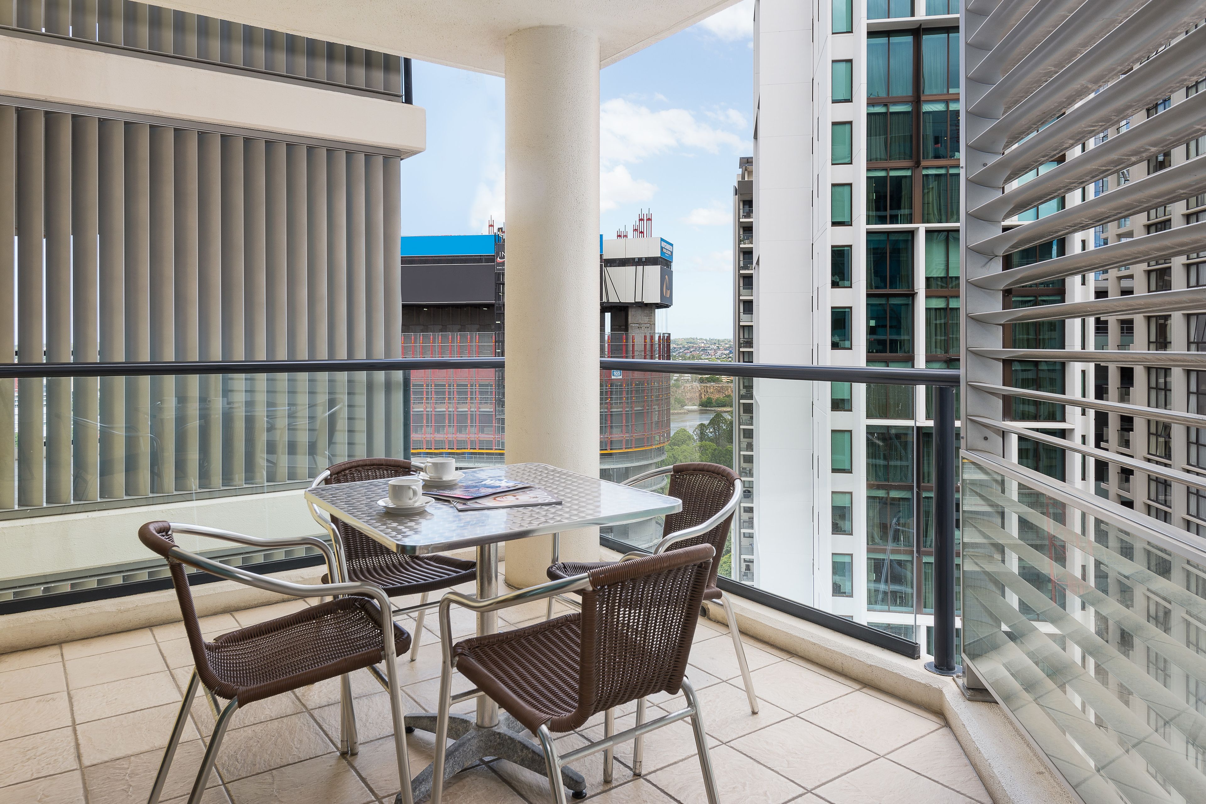 Ein Balkon mit Glastisch und Korbstühlen, der auf einen Stadtblick mit modernen Gebäuden blickt.