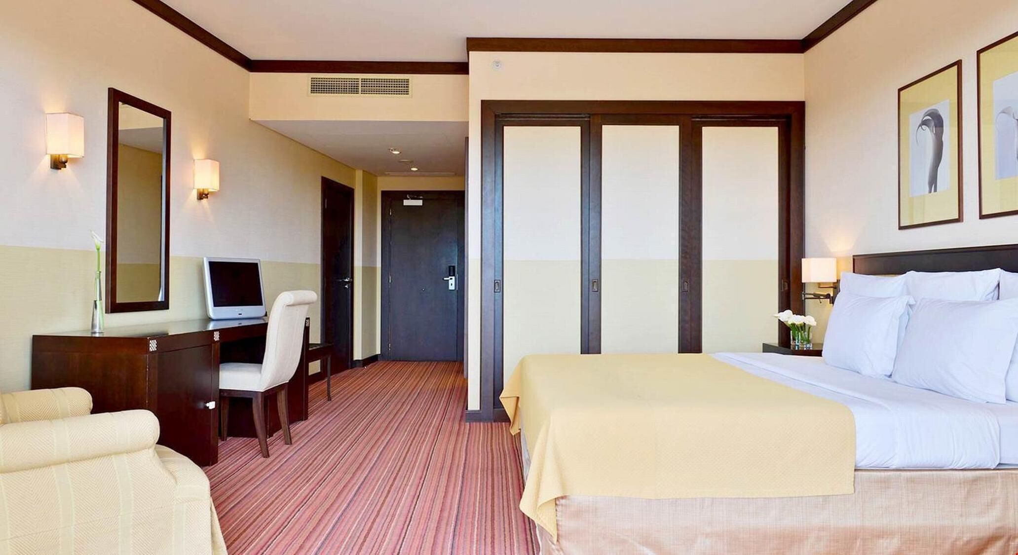 Een hotelkamer met een bed, bureau, stoel en een grote spiegel.