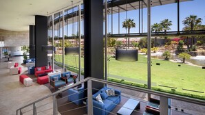A spacious living area with modern furniture, large windows offering a view of a landscaped garden and palm trees. - Pestana Vila Sol Golf - Vilamoura (Loulé)