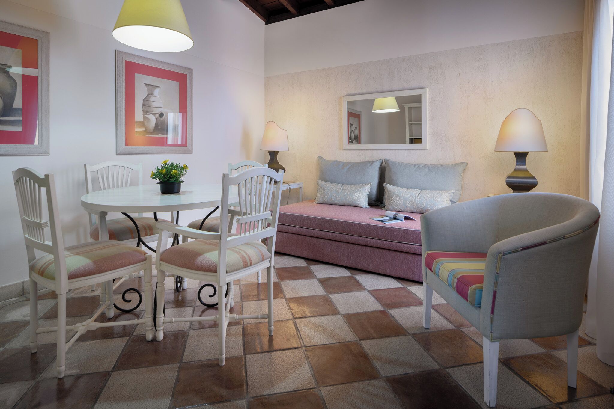 A dining area with a round table, white chairs, a small potted plant, and a pink sofa.