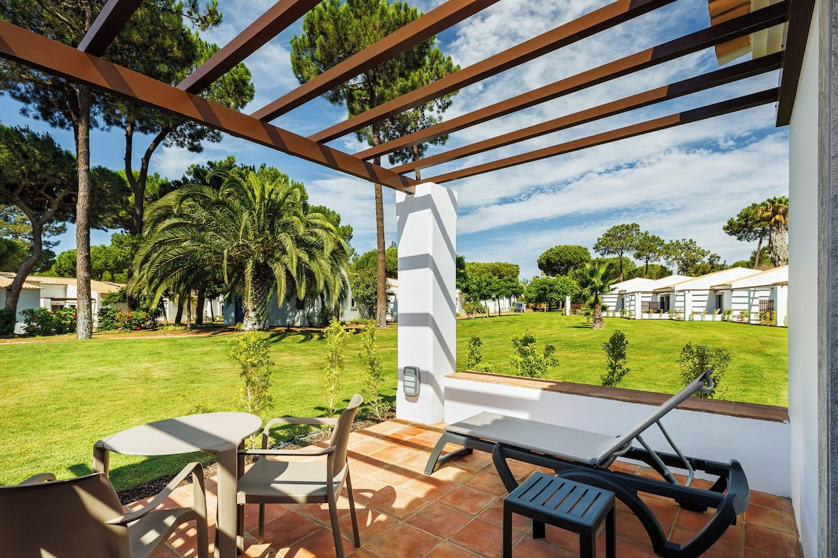 Une terrasse extérieure avec une table et des chaises, une pergola et une vue sur une pelouse et des arbres bien entretenus.