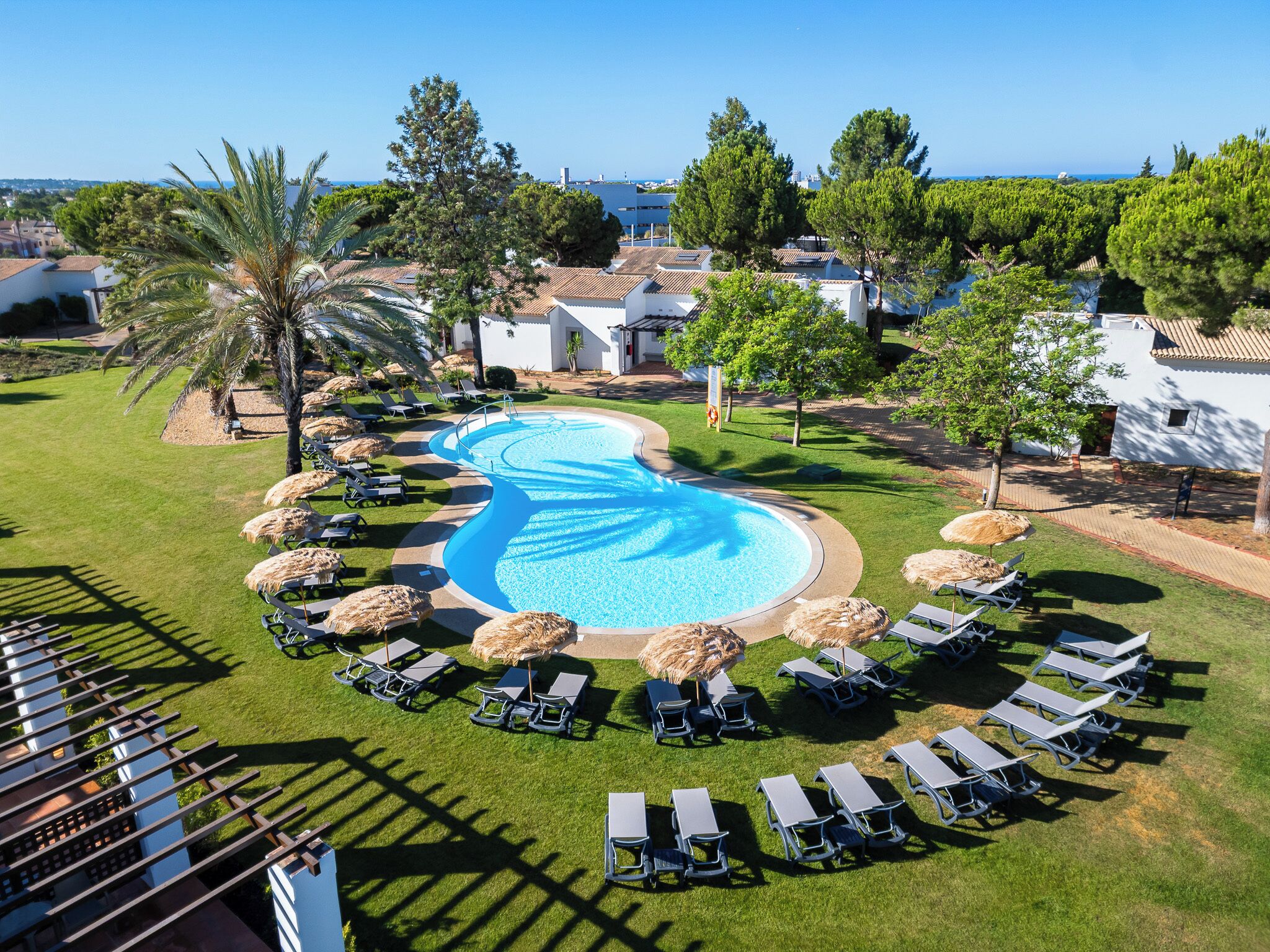 Un resort con una piscina grande, tumbonas y vistas al mar.