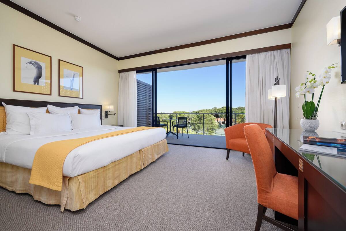 Une chambre d’hôtel avec un grand lit, un bureau, une chaise et un balcon offrant une vue sur le paysage.